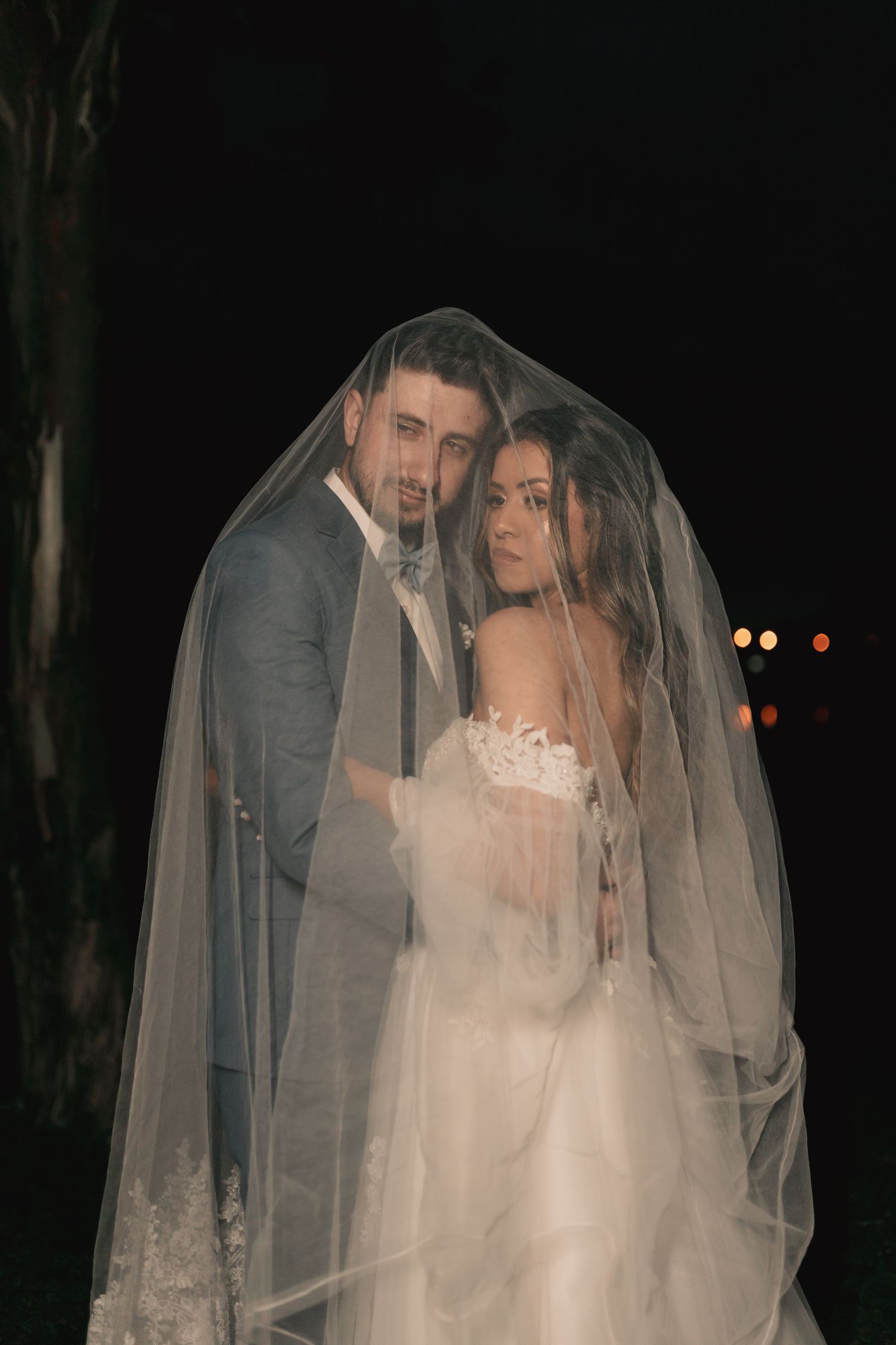 Bride and groom sharing a quiet moment under a veil at night